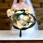 "دسته گل عروس مینیمال، طراحی ساده و شیک از گل‌های ارکیده سفید و برگ‌های سبز برای عروس‌هایی که زیبایی و سادگی را ترجیح می‌دهند."