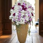 "تصویری از جام گل طلایی ارکیده با طراحی شیک و گل‌های سفید و بنفش از گلفروشی فلورانس"