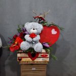 خرس مهربان رز قرمز دردست ولنتاین - خرس عروسکی کرم رنگ با پاپیون قلبی، رز قرمز هلندی در دستان خرس، هدیه عاشقانه لطیف از گلفروشی فلورانس